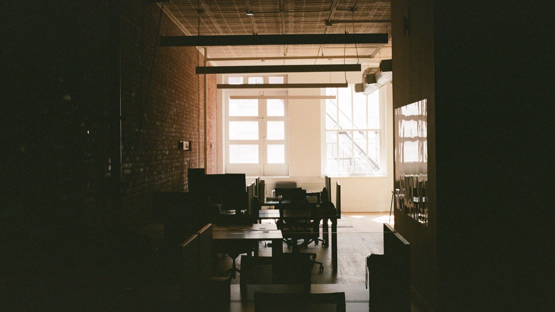 The SEA12 office — desks along an exposed brick wall, tall windows at the far end.